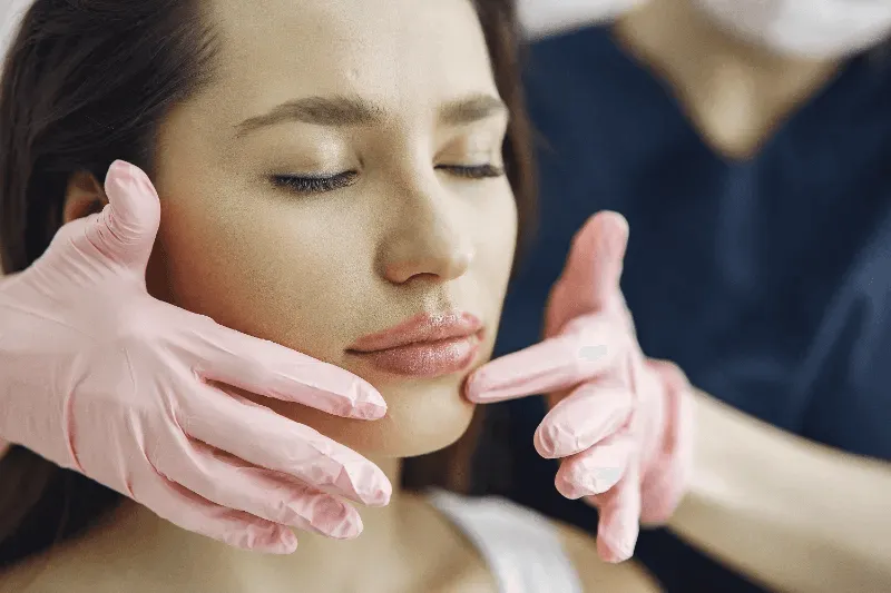 The image shows a professional examining a client's lips after a cosmetic procedure.