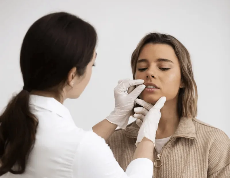 The image depicts a professional examining a client's lips, indicating a consultation process to discuss what to expect during and after a cosmetic procedure.