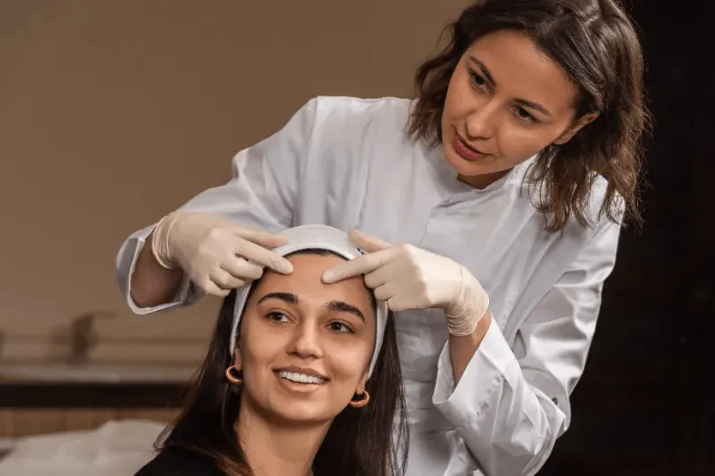 The image shows a professional providing a consultation to a smiling client, representing aftercare tips for permanent eyebrow treatments.