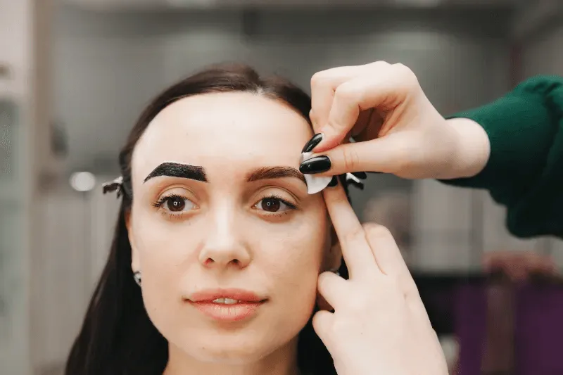 This image depicts a woman undergoing the process of permanent brow shaping.