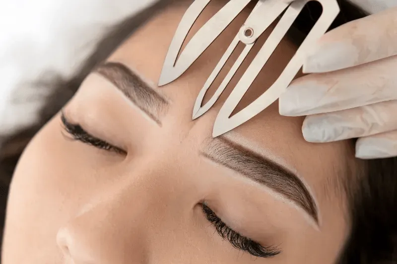 A professional carefully measures eyebrow symmetry with precision tools for flawless brow lamination.